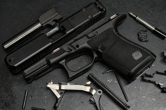 TALLINN, ESTONIA - FEBRUARY 18, 2026: Disassembled Glock 19 Gen 6 semi-automatic pistol parts, slide, and frame on a dark workbench.