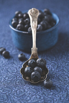 Spoon of Blueberries Propped Up on a Small Blue Bowl on a Blue Fabric Background
