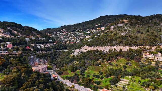 Cityscape and lush greenery covers the mountain slopes. Approaching the picturesque scenery of Nice, France from drone.