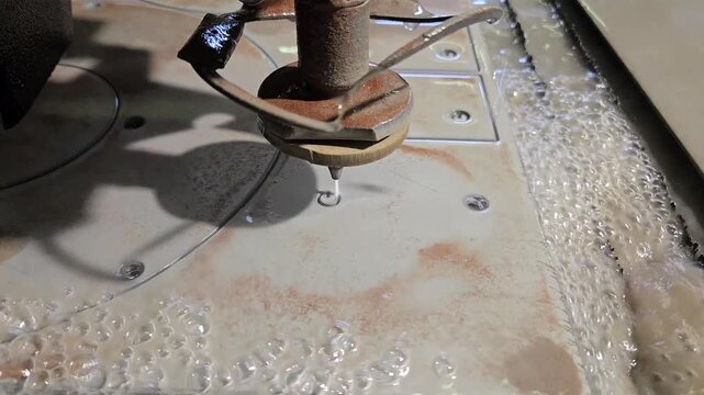 4K Macro of CNC waterjet machine cutting steel plate with brown garnet abrasive sand in industrial workshop