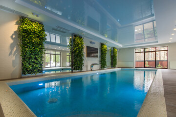 Obraz premium This space features a swimming pool surrounded by greenery. Large windows allow natural light to enter, creating a bright and open area for relaxation and leisure activities