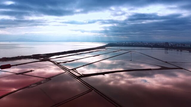 Aerial view of geometric pink salt evaporation ponds. High angle shot of pink and blue salterns reflecting sky with sun rays.