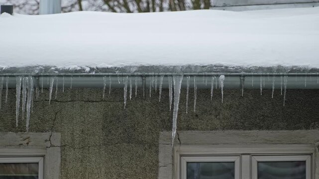 Long Hazardous Icicles Hanging from Frozen Rain Gutter Over Street Sidewalk Posing Injury Danger for Pedestrians