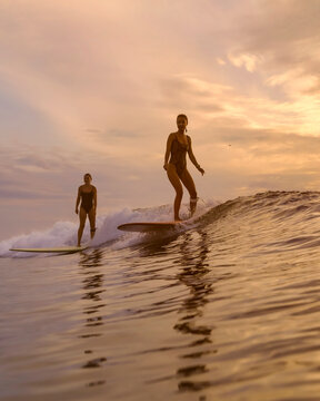 Two Surfers Riding Sunset Wave, Woman And Companion Gliding Longboards, Golden Light, Reflective Water, Calm