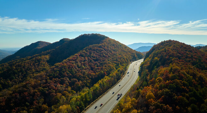 Aerial view of I-40 freeway in North Carolina leading to Asheville through Appalachian mountains in golden fall with fast moving trucks and cars. Interstate transportation concept