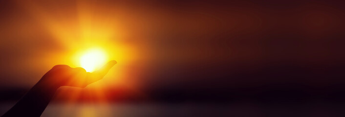 Sun on hand on orange sunset background. Silhouette of palm holding sun. Long banner