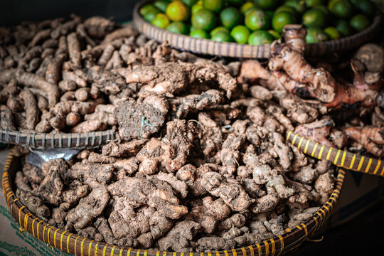 Turmeric, ginger, and temulawak (Javanese ginger) displayed on a wooden tray at a traditional market, sold as natural ingredients for herbal medicine or jamu