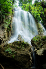 Detailed view of the tiered cascades at Pelang Waterfall. Natural spring water trickling through dense tropical foliage and mossy cliff walls.