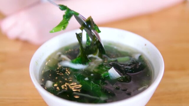 white bowl of miso soup. It is traditional japanese food. Main ingredients are miso paste, tofu, wakame seaweed and shiitake mushrooms.