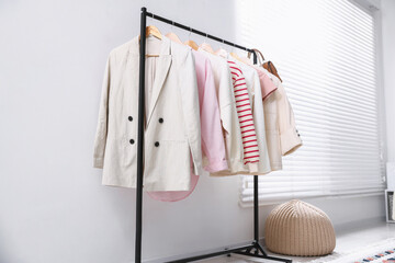 Different stylish clothes hanging on rack indoors