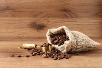 Coffee beans, scoop and sack on wooden table, closeup