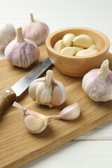 Fresh garlic bulbs, cloves and knife on white wooden table, closeup