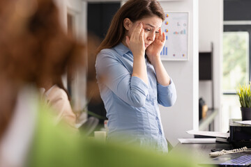 Fototapeta premium Stressed professional woman touches head in frustration and analyzes marketing strategy files on digital device. Tired employee experiences pressure and anxiety in busy workplace.