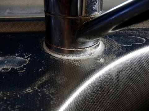 Hard water calcium stains and limescale on stainless steel kitchen sink faucet.