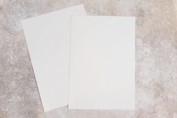 Two sheets of blank watercolor paper mockup placed on a textured surface, showcasing their smooth, unmarked surfaces for artistic design and presentation purposes