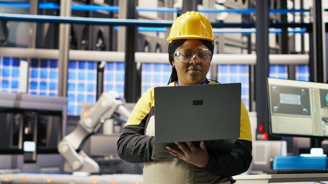 Engineer performing predictive maintenance using laptop, analyzing IoT sensor data, managing operational reliability of photovoltaic systems in smart factory environment, camera B