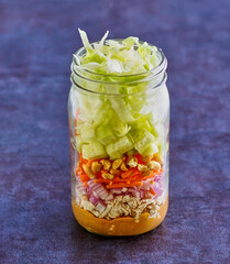 thai style chicken mason jar salad with shredded lettuce, red onion, carrots, and peanuts