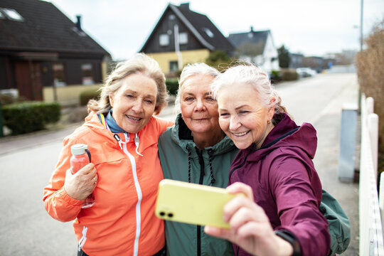 Three senior women friends taking selfie on suburban street