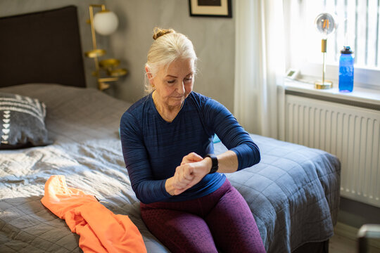 Active senior woman checking fitness watch in home bedroom