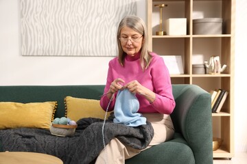 Obraz premium Senior woman knitting with needles on sofa at home