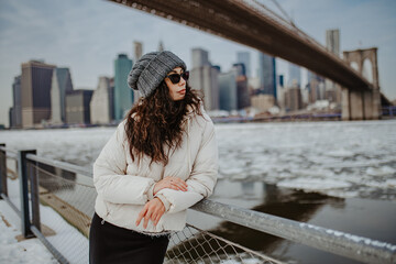 Profile portrait of woman in winter hat at bridge. Side view of woman in white jacket and grey beanie looking at city skyline across the water. © white78