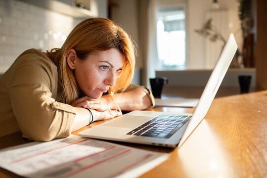 Worried woman reviewing bills on laptop at kitchen table