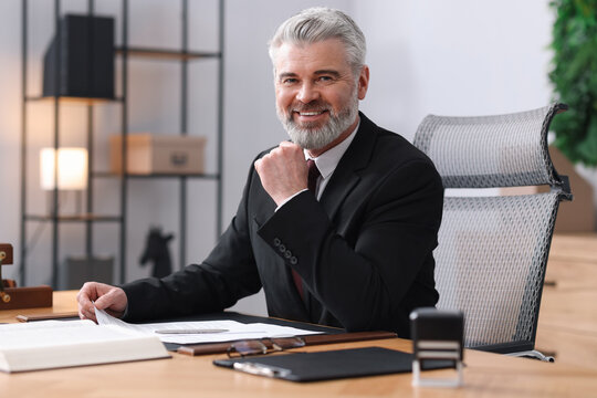 Portrait of smiling notary in suit with documents at table in office