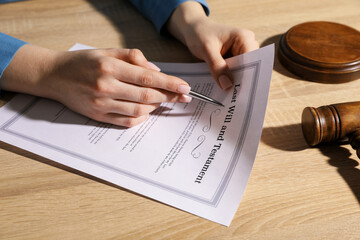 Woman signing Last Will and Testament at wooden table indoors, closeup