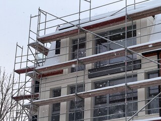 Fototapeta premium Building under construction with scaffolding covered in snow during winter. Cold weather impact on new residential or commercial development.