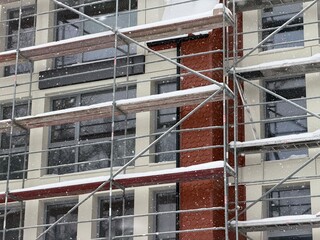 Building under construction with scaffolding covered in snow during winter. Cold weather impact on new residential or commercial development.