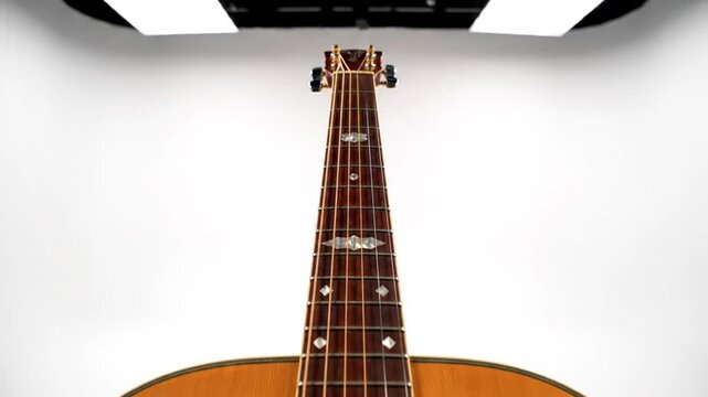 Close-up perspective of a beautiful wooden acoustic guitar neck with intricate fret markers and strings against a white background.