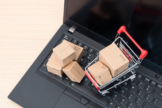 Top view of shopping cart filled with small parcel boxes on laptop keyboard. Internet shopping platform, ecommerce transaction, product shipment, online retail strategy, business growth concept.