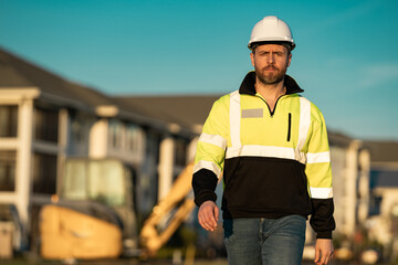 Caucasian man, construction worker in helmet at construction site. Industry engineer worker in hardhat near bulldozer or digger tractor. Concept of construction industry. Construction site manager. © Olena