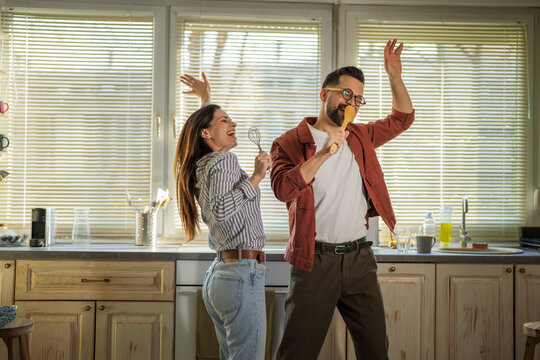 Happy couple singing and dancing while cleaning kitchen