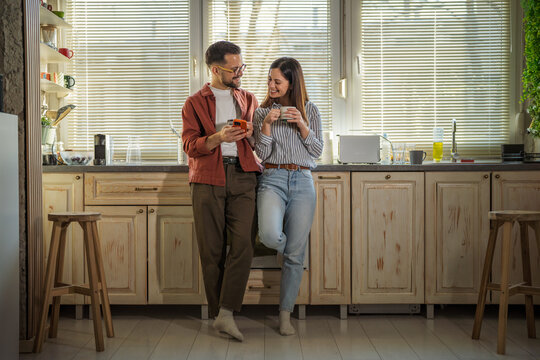 Couple enjoying morning coffee and smart phone in kitchen