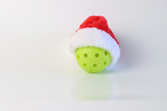 A single lime green pickleball is adorned with a classic red and white Santa hat, ready for Christmas-themed athletic activities
