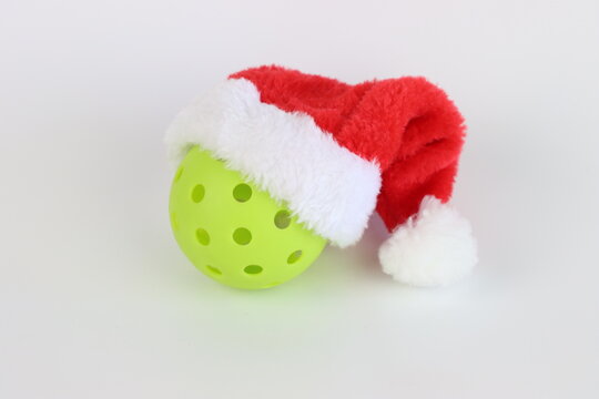 A single lime green pickleball is adorned with a classic red and white Santa hat, ready for Christmas-themed athletic activities