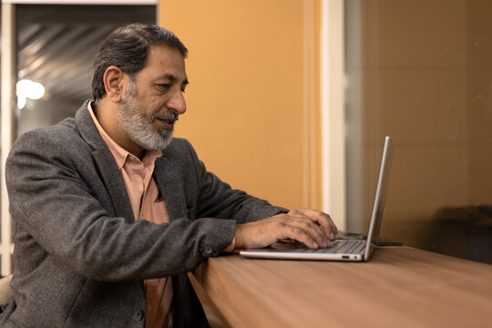 Indian senior businessman sitting  in front of a laptop in office