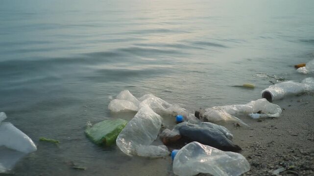 Plastic waste scattered on the beach shoreline with calm water in the background viewed from a low angle