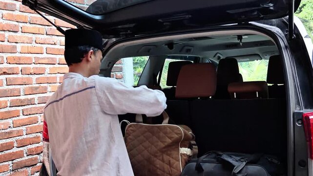 An Asian Muslim man puts his bag in the trunk of his car. Preparations for the Eid homecoming.