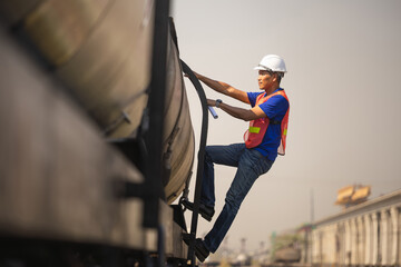 Industrial engineer performing a safety check on a fuel tanker train at a railway yard, Railway worker in safety vest climbing a freight tank wagon to inspect cargo during a logistics operation