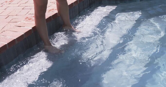 Woman is stepping into yard pool bench, splashing, then tossing striped beach ball overhead to play
