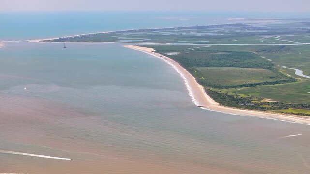 Panoramic aerial view of island beach landscape and marshes near Charleston, South Carolina showcasing lowcountry beaches and waterways with Morris Island Lighthouse in the distance - 4K Drone