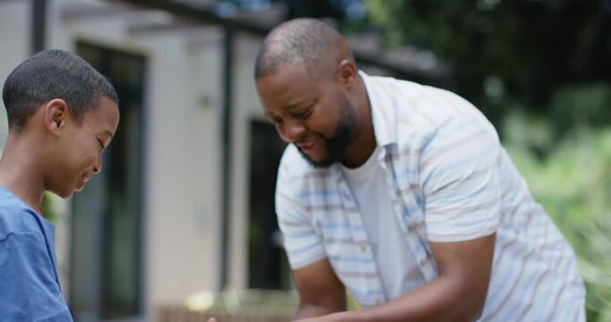 Spotting tuber on patio table, African American dad guiding and handing it to teenage son, teaching