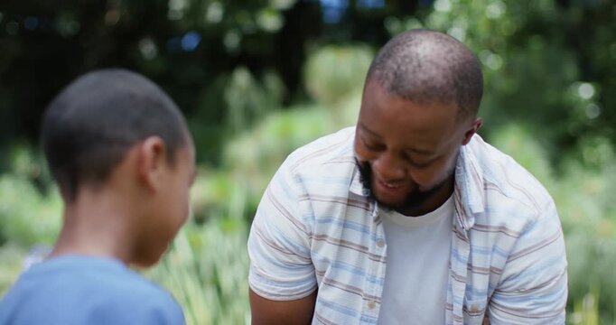 African American dad with son offering purple tuber dad wearing striped shirt inspecting in garden
