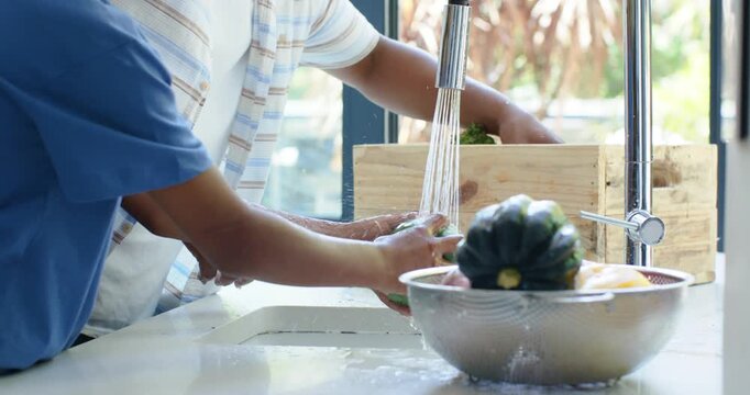 Running faucet is causing parent-child rinsing produce at sink, placing into basket for cooking