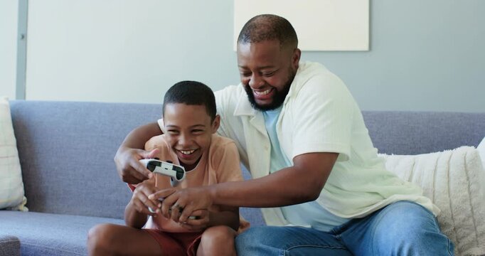 Father and child laughing dad reaching for controller guiding hands playing with gamepads on couch
