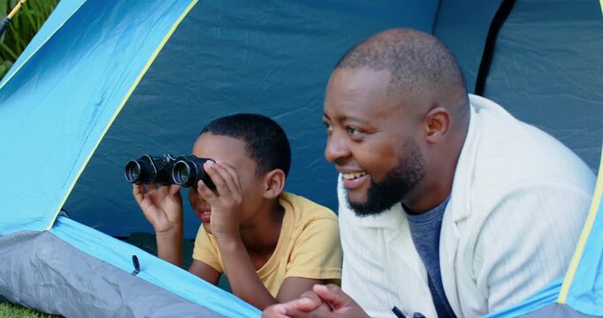 Father and boy responding to motion outside blue tent, boy in yellow shirt scanning with binoculars