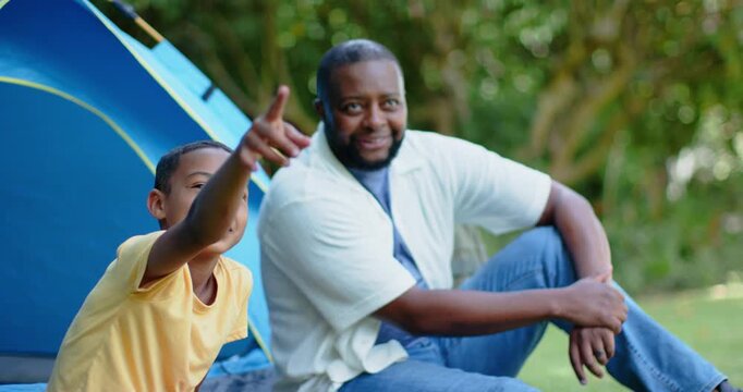African American father and son boy pointing, sharing discovery and high-fiving beside blue tent
