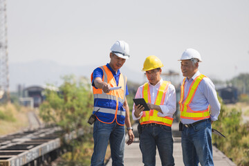 Professional engineering team in safety vests and hardhats using a digital tablet conducting a site inspection and discussing logistics infrastructure development at a railway yard